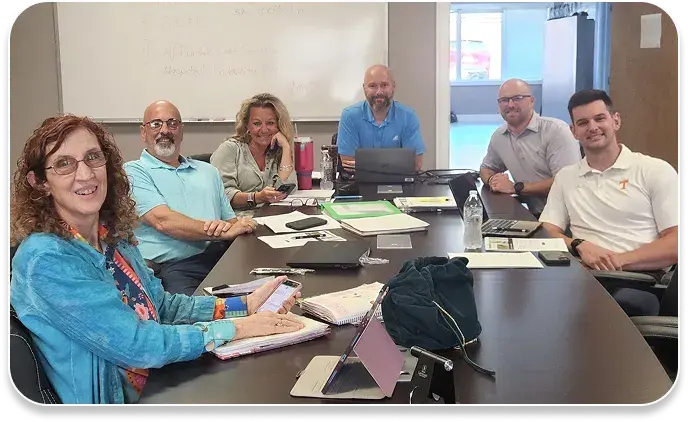image shows men & women seated at a conference table, smiling at the camera